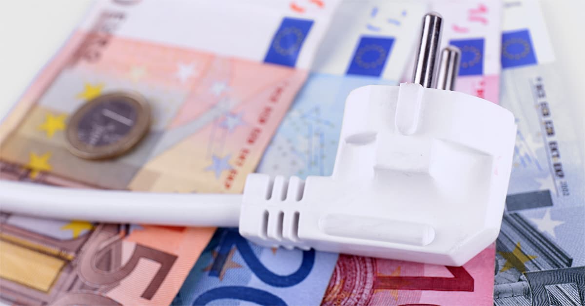 Enchufe eléctrico blanco sobre billetes y monedas de euro, representando el coste de la electricidad y el ahorro energético.